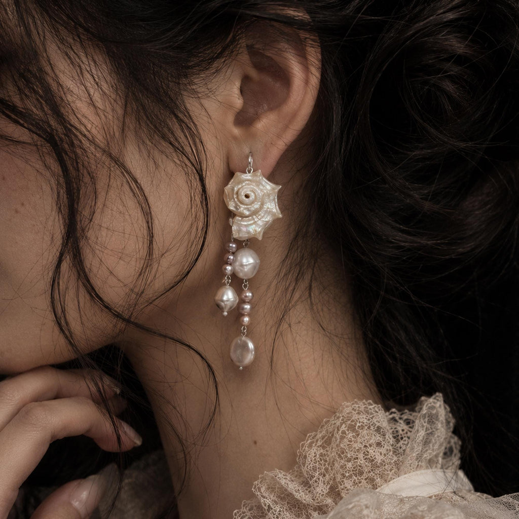 Long conch-shell earring with several pale bead drops shown worn beside lace.