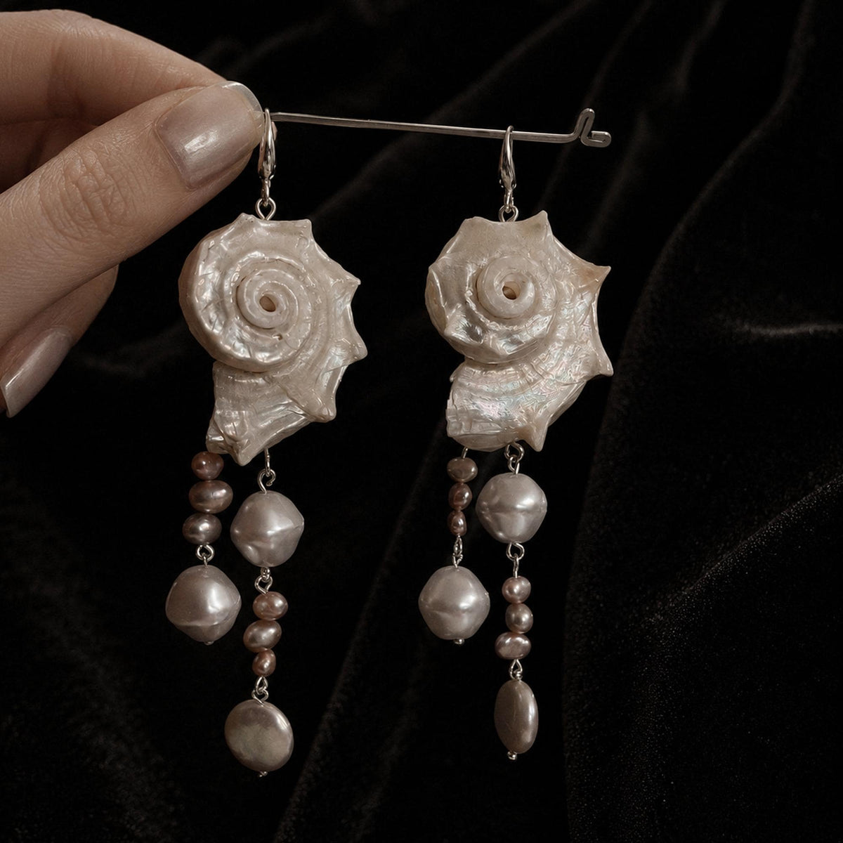 Pair of long spiral conch-shell earrings with pale bead drops suspended from a metal bar.