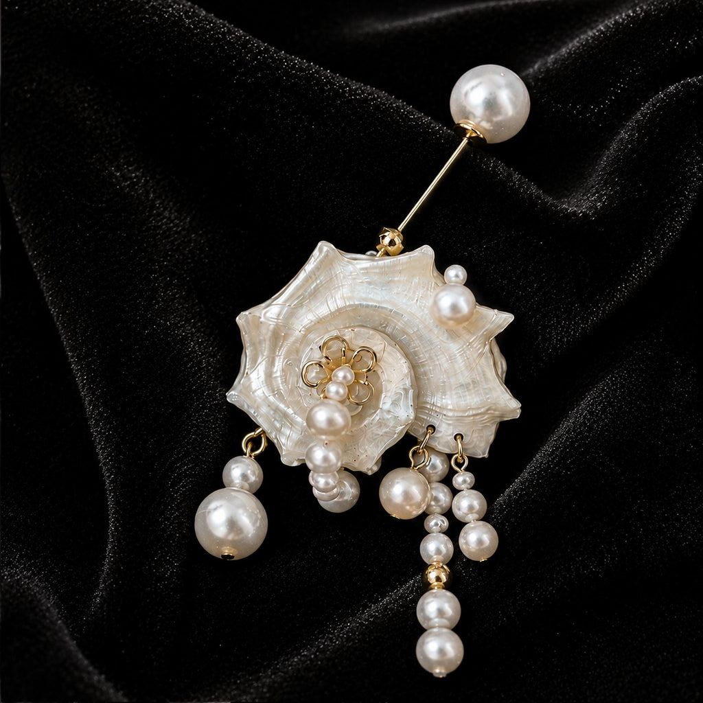 Conch-shell brooch with bead drops and a long pearl-topped pin on black velvet.