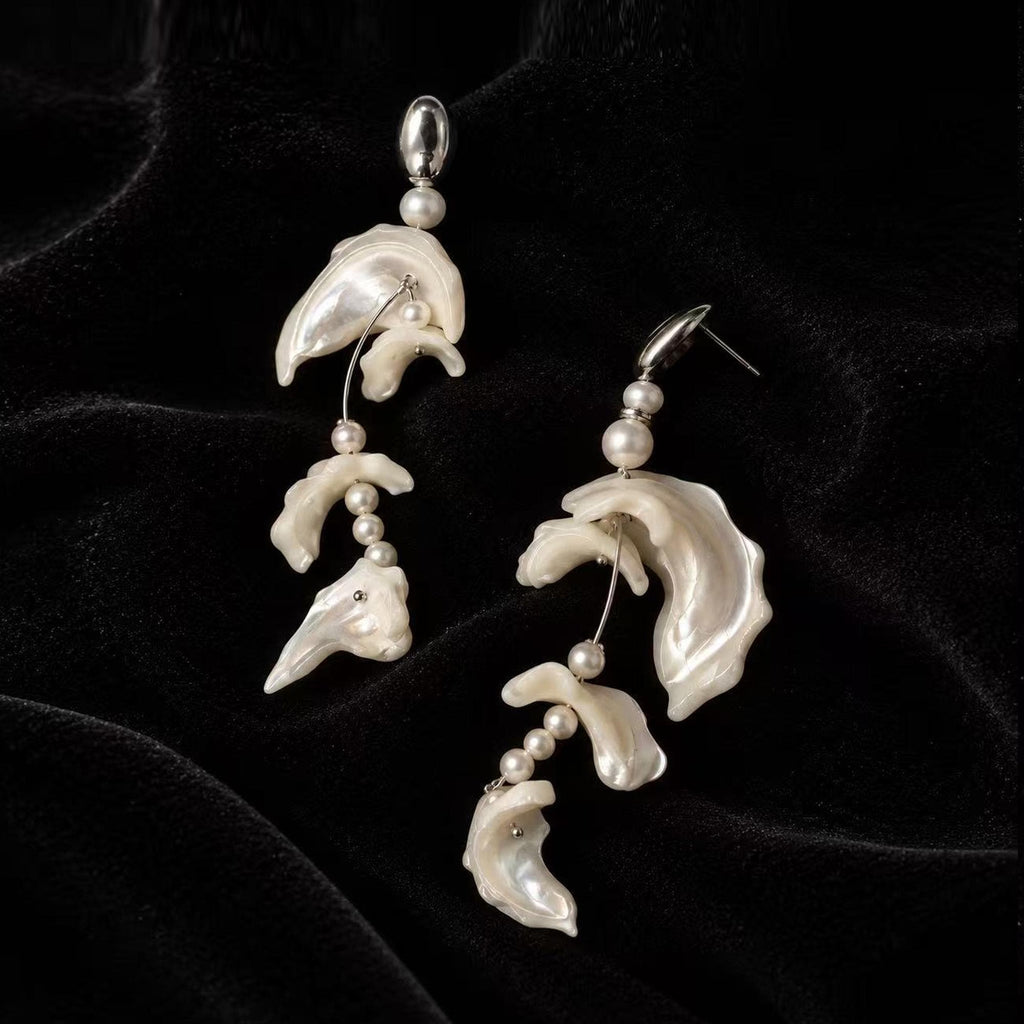 Pair of asymmetric shell-fragment earrings with pale wavy sections on black velvet.