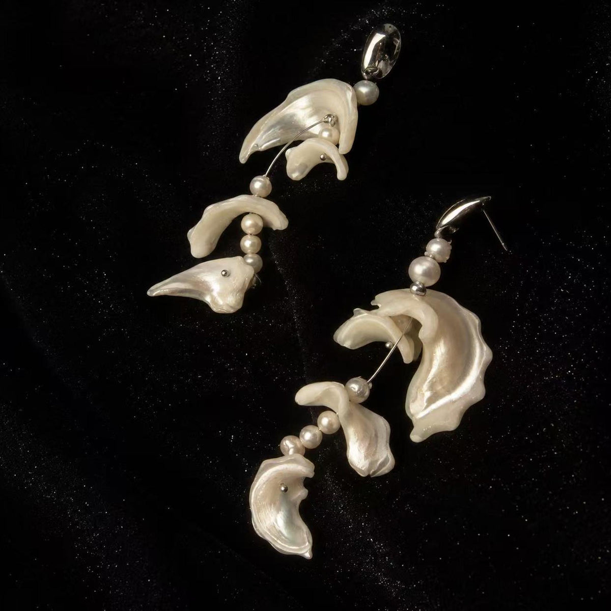 Close view of shell-fragment earrings showing curved pale pieces and bead connections.