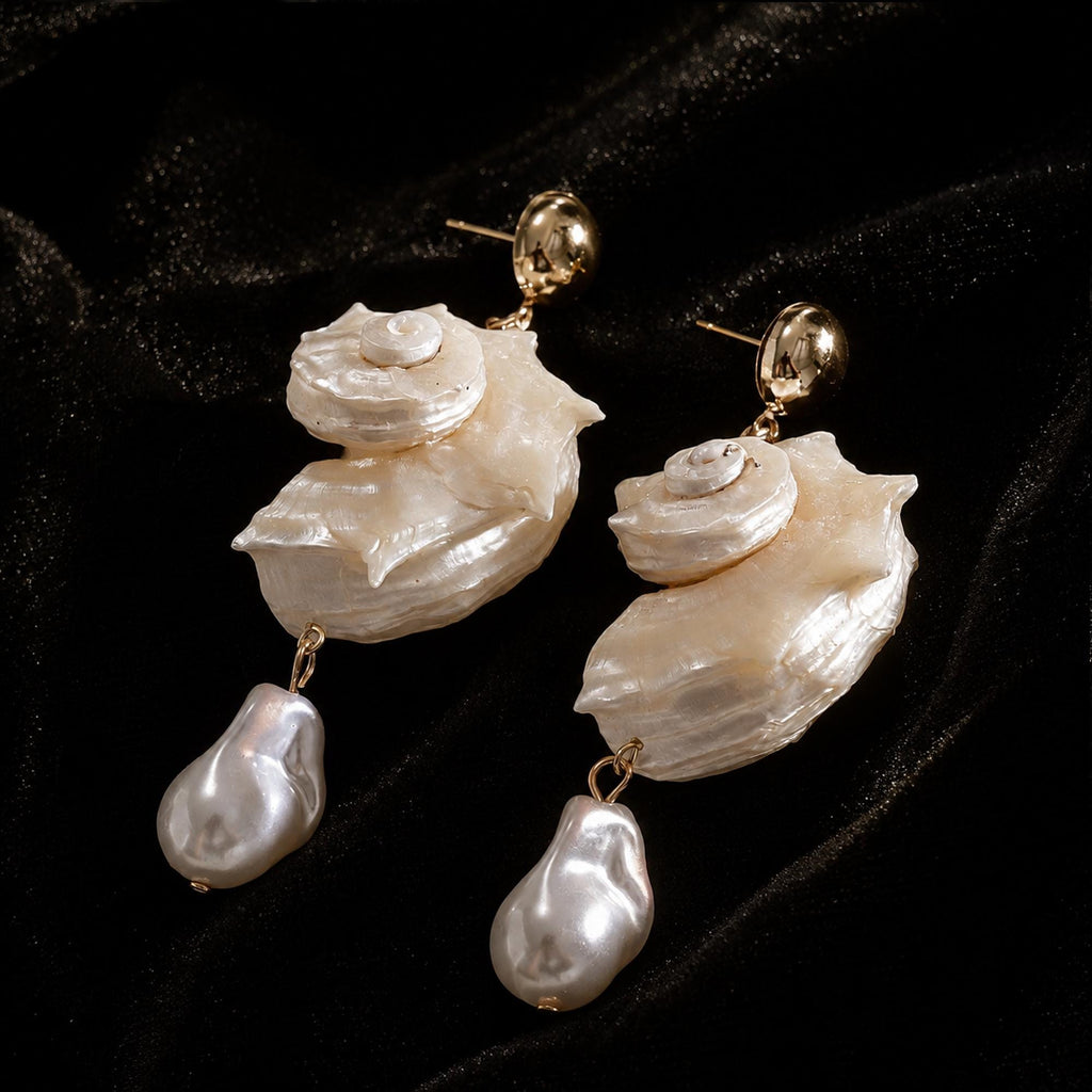 Pair of spiral conch-shell earrings with large pale teardrop beads on black velvet.