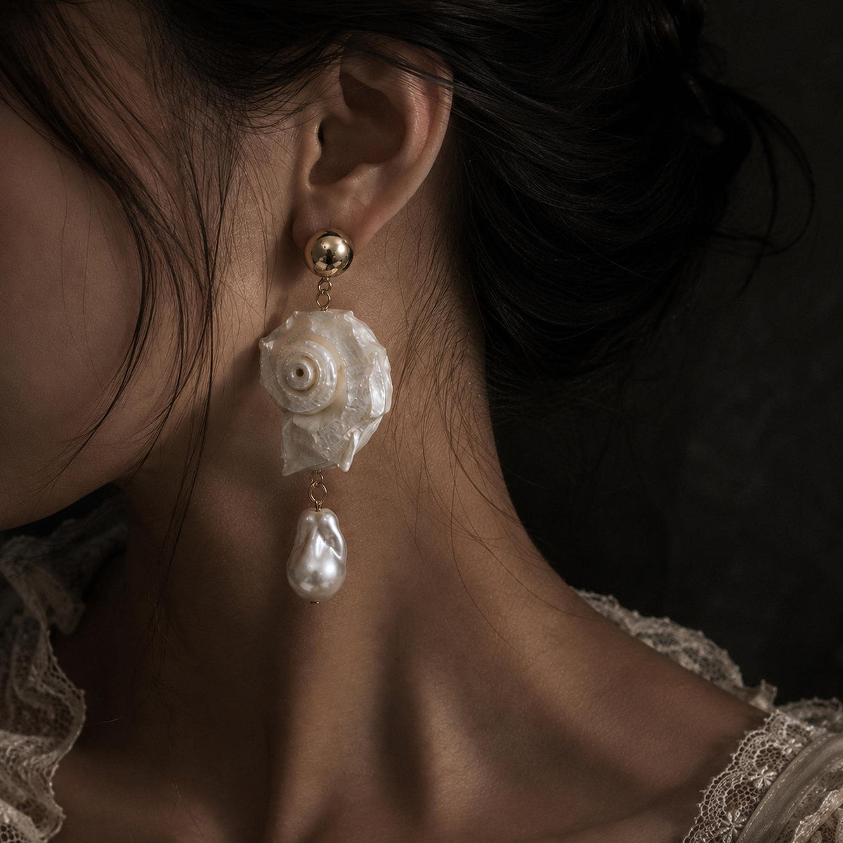 Spiral conch-shell earring with a large pale teardrop bead, shown worn.