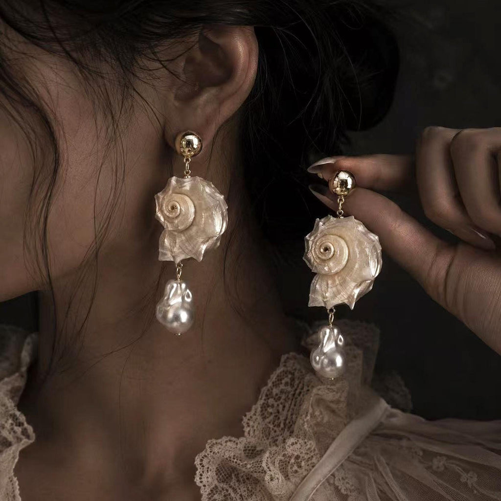 Spiral conch-shell earring shown worn while the matching earring is held beside it.