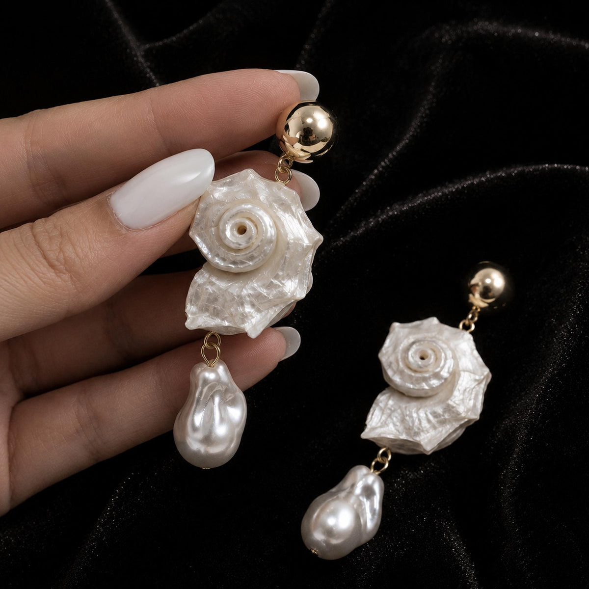 Spiral conch-shell earrings with large pale teardrop beads, held in a hand.