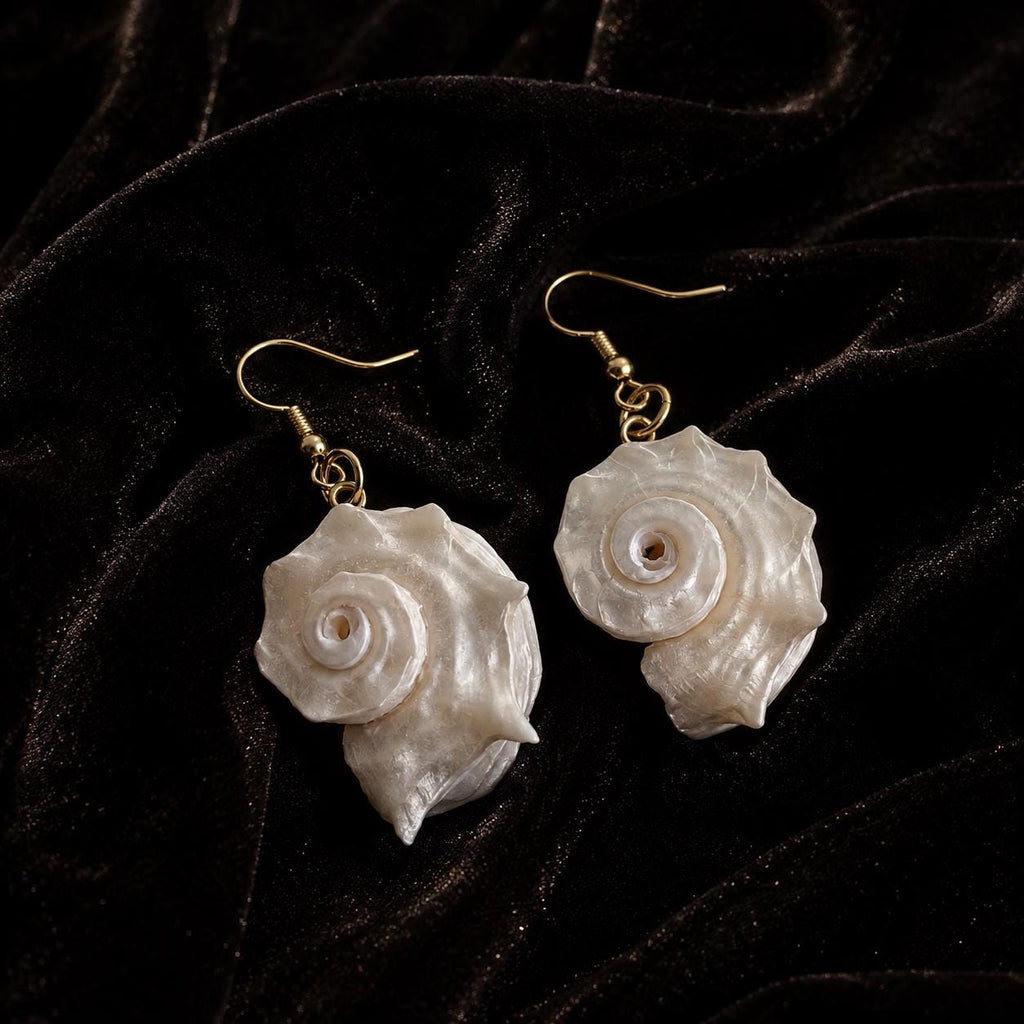 Close view of spiral conch-shell drop earrings showing their pale iridescent surfaces.