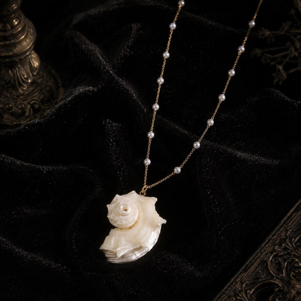 Close view of an iridescent conch-shell pendant and delicate bead-accented chain.