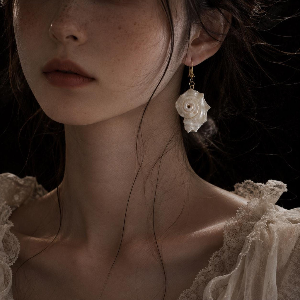Natural iridescent conch-shell earring worn beside an ivory lace neckline.