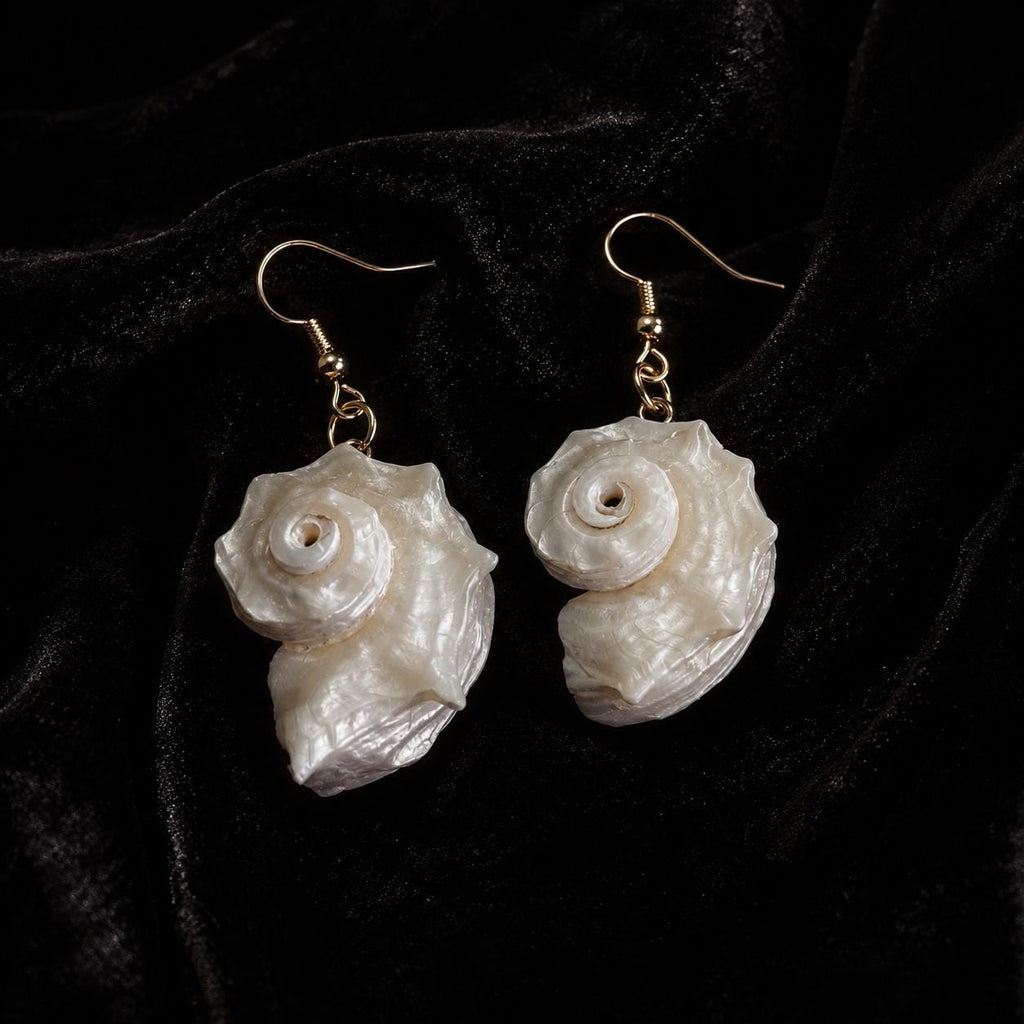 Pair of pale spiral conch-shell drop earrings with gold-tone hooks on black velvet.
