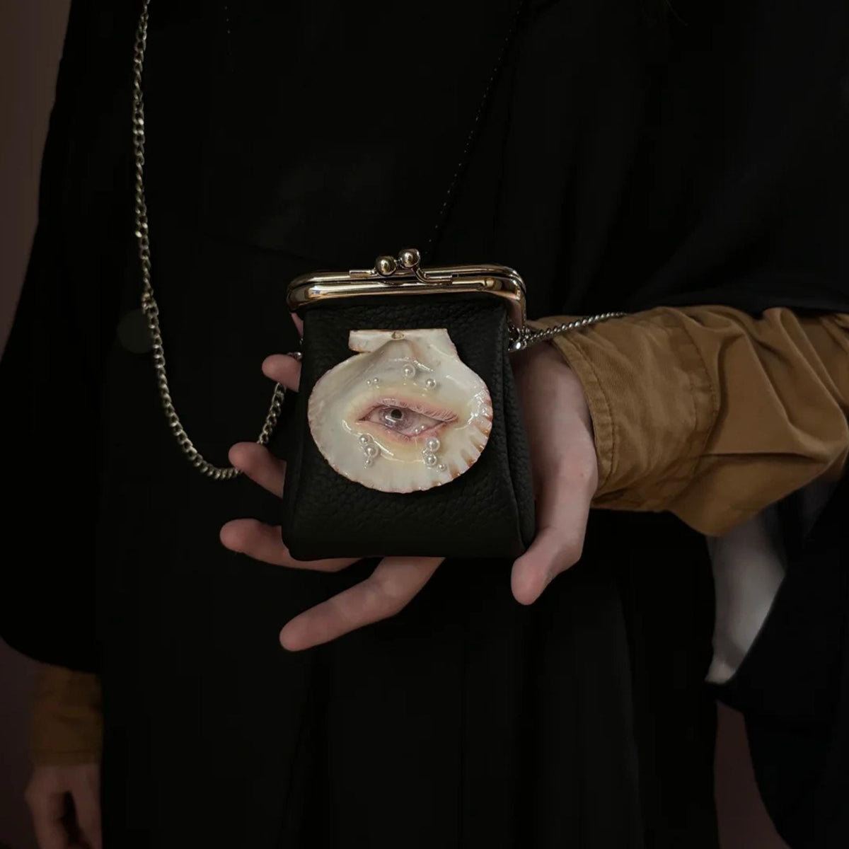 Black Oyster Eye Mini Crossbody Bag held in a hand against a dark outfit.