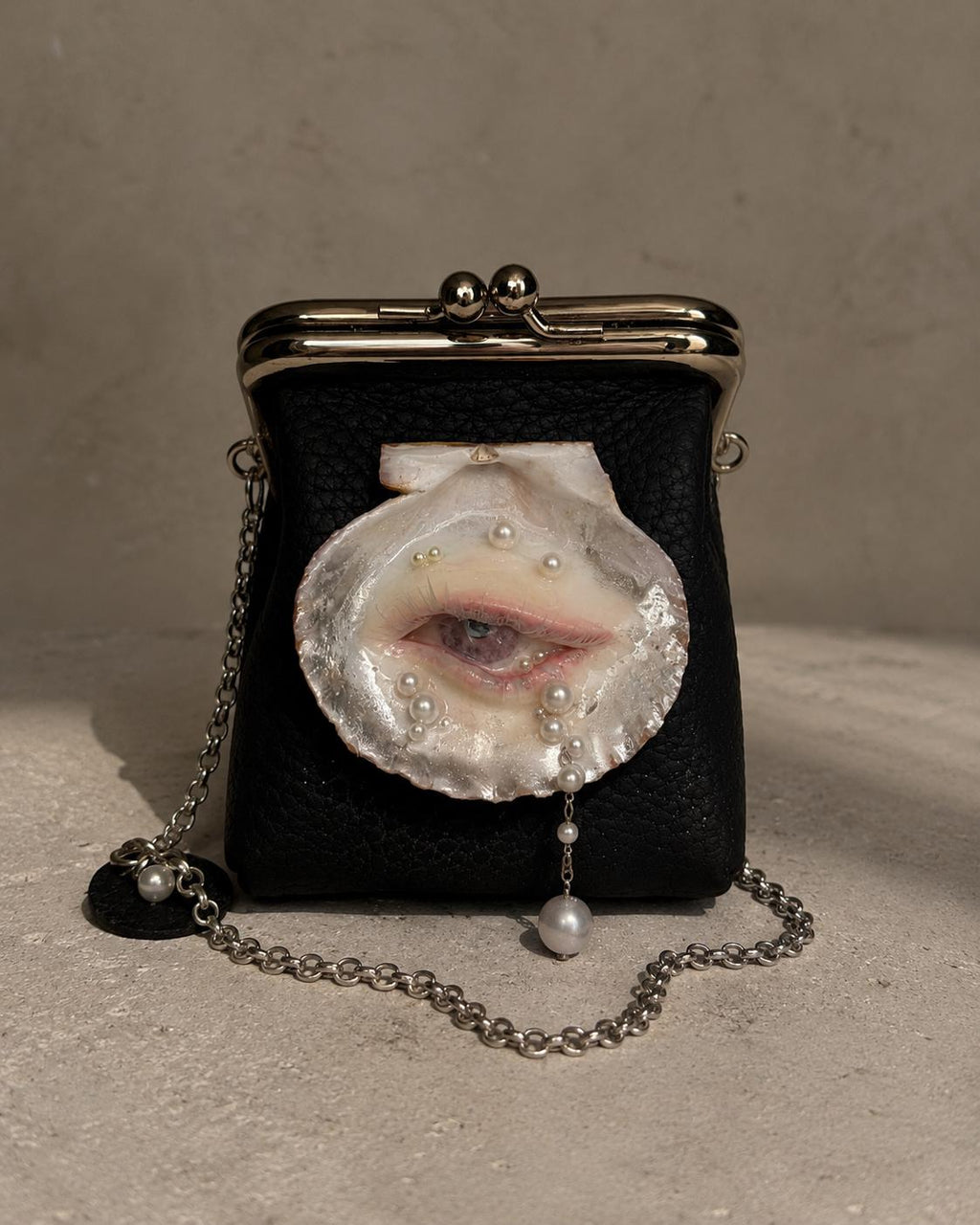 Black Oyster Eye Mini Crossbody Bag standing on a pale surface with its chain beside it.