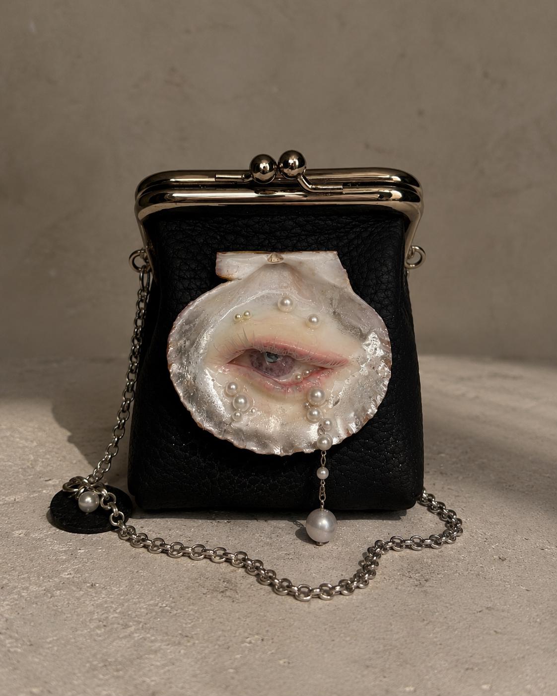 Black Oyster Eye Mini Crossbody Bag standing on a pale surface with its chain beside it.