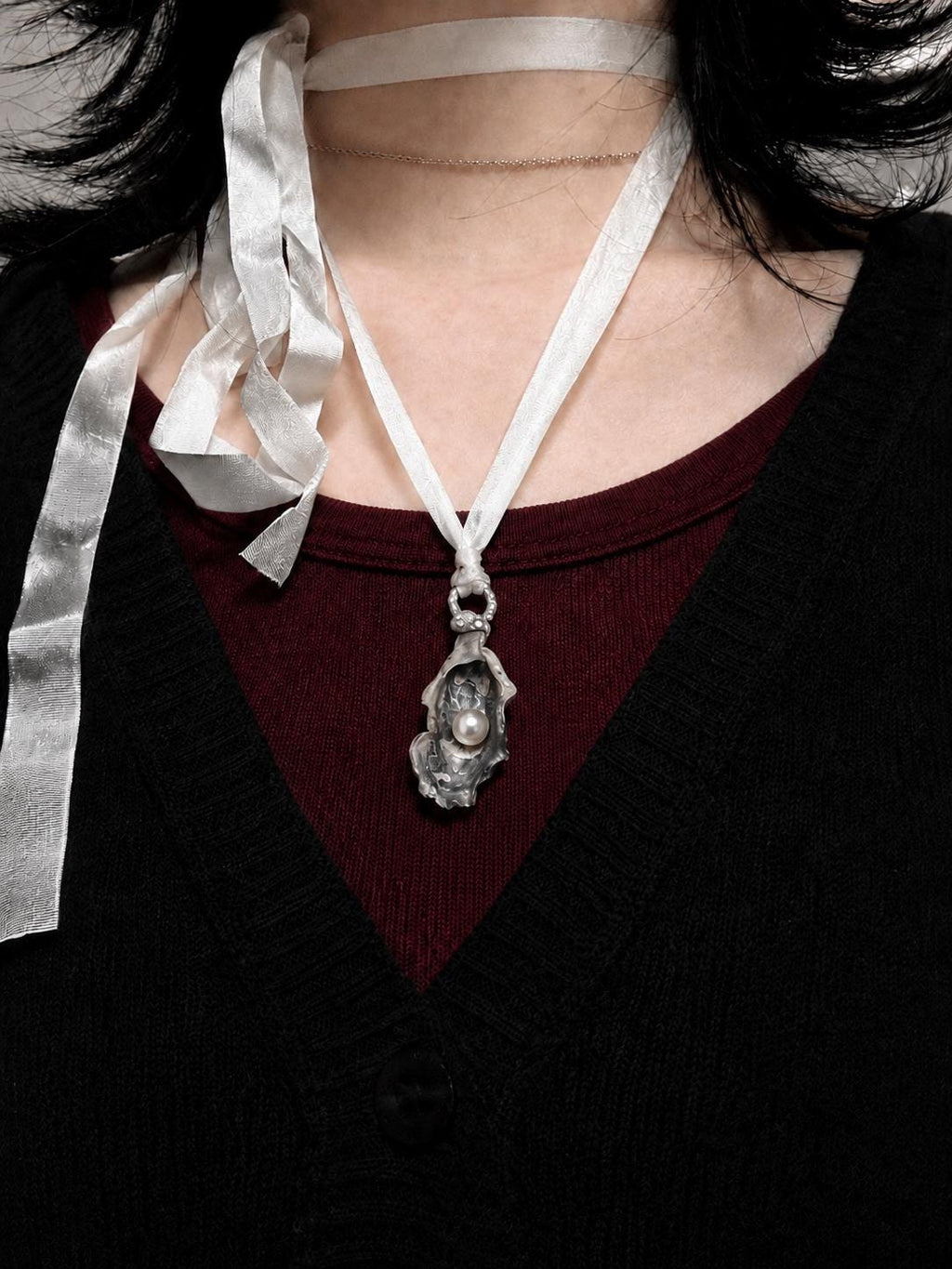 Shell Pearl Talisman pendant worn on ivory ribbon over a dark red top.
