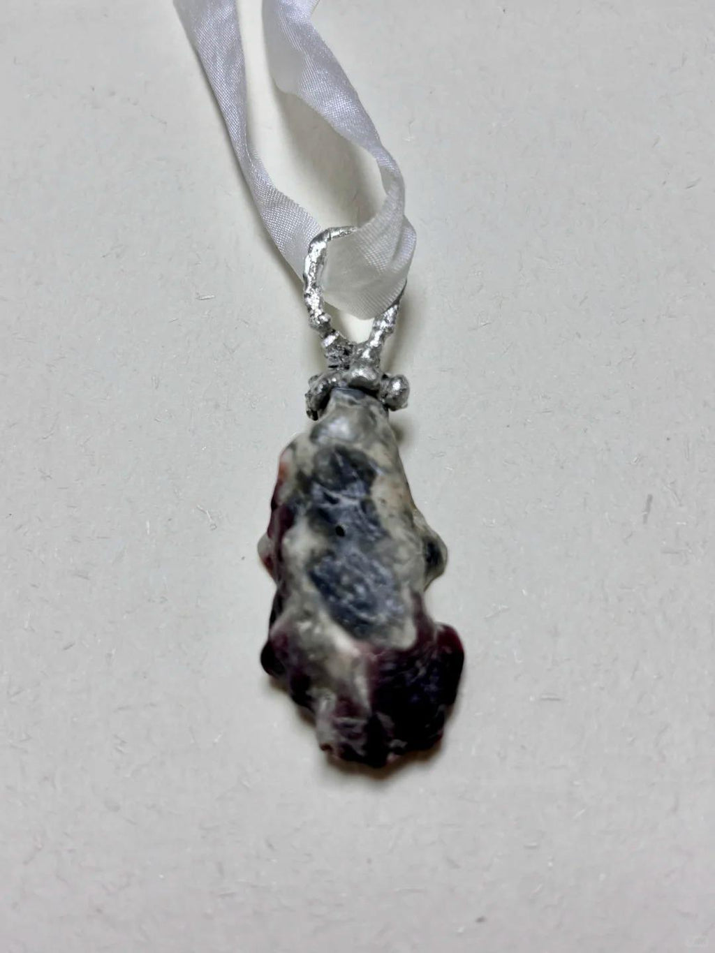 Shell Pearl Talisman pendant hanging vertically from ivory ribbon.