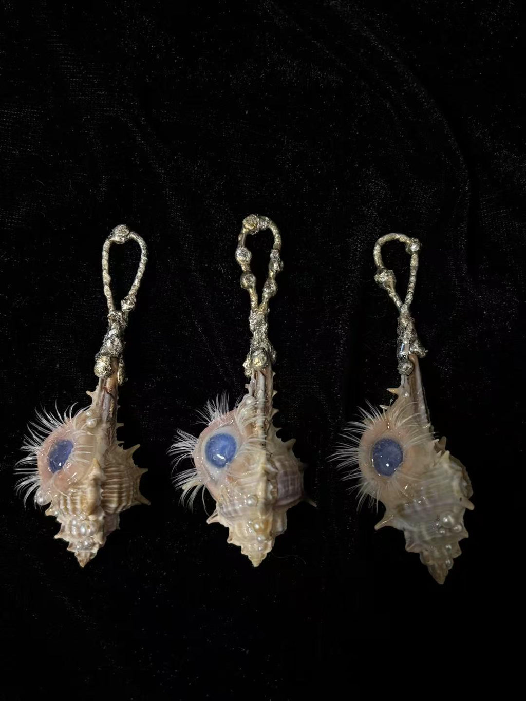 Three Conch Eye Talisman variations with blue irises displayed on black fabric.