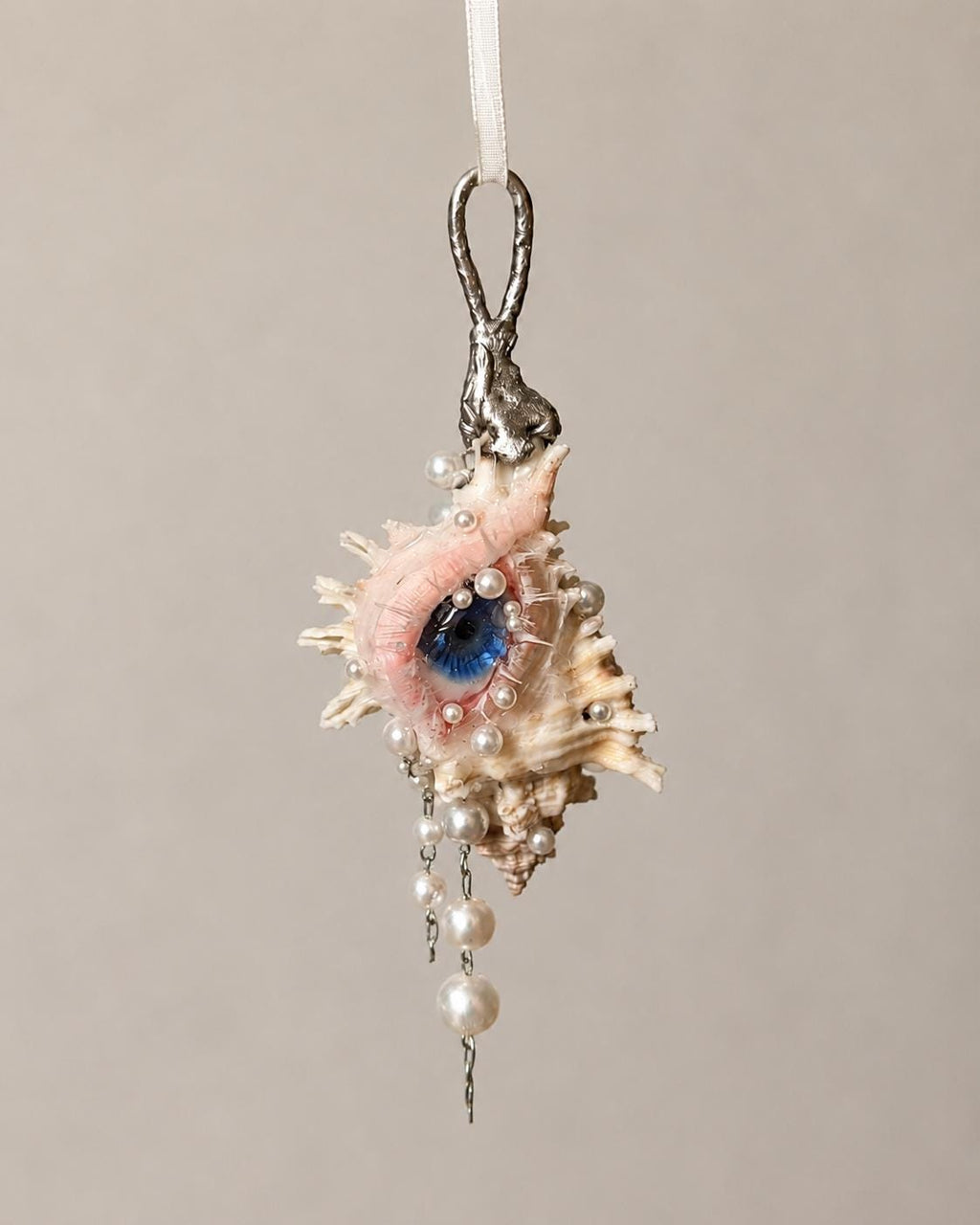 Conch Eye Talisman hanging from a metal attachment, showing a blue eye and pale bead drops.