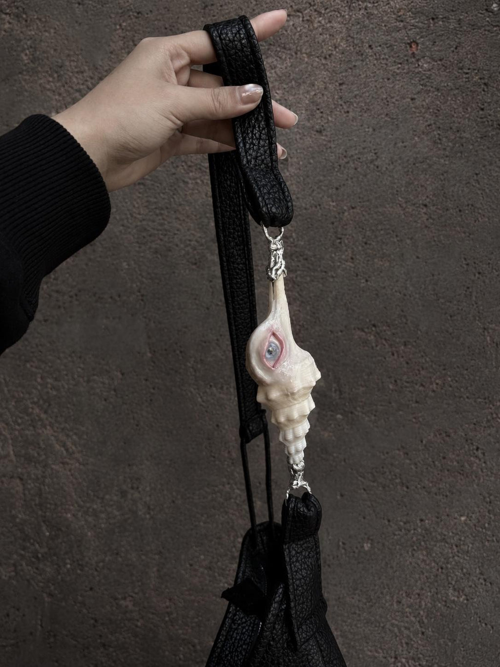 Long Conch Eye Shoulder Bag held by its extended strap to show its full shape.