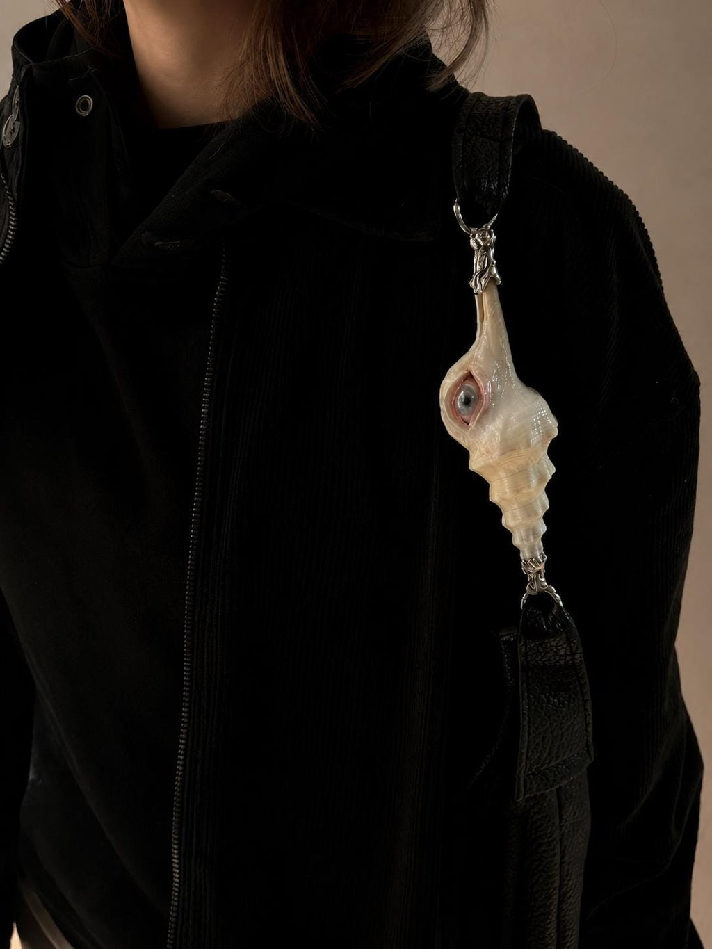 Close view of the Long Conch Eye Shoulder Bag strap and shell-eye ornament against a black outfit.
