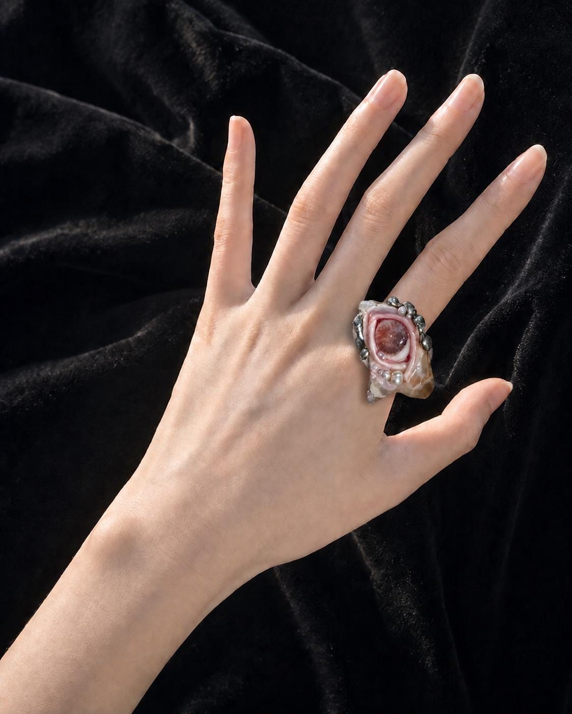 Shell-eye statement ring worn on an outstretched hand against black fabric.