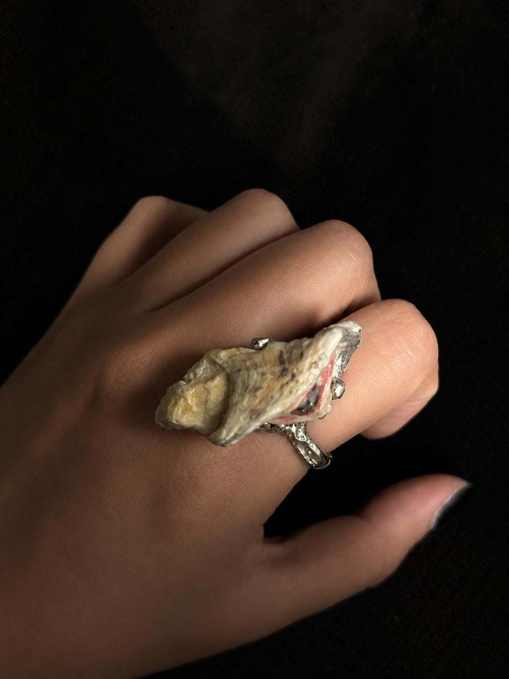 Back of a shell-eye ring worn on a finger, showing the natural shell exterior.