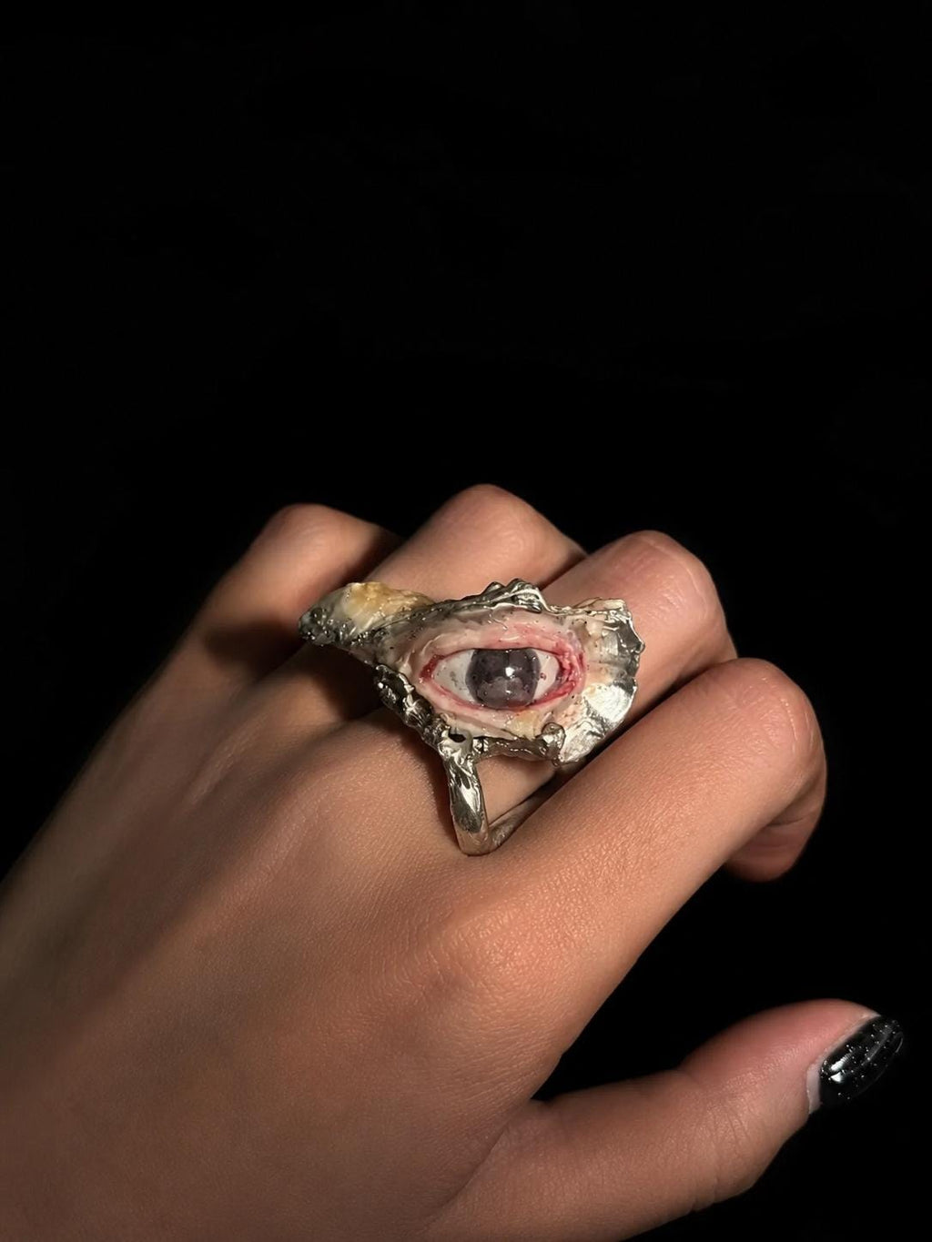 Brown-eyed shell statement ring worn on a hand against a dark background.