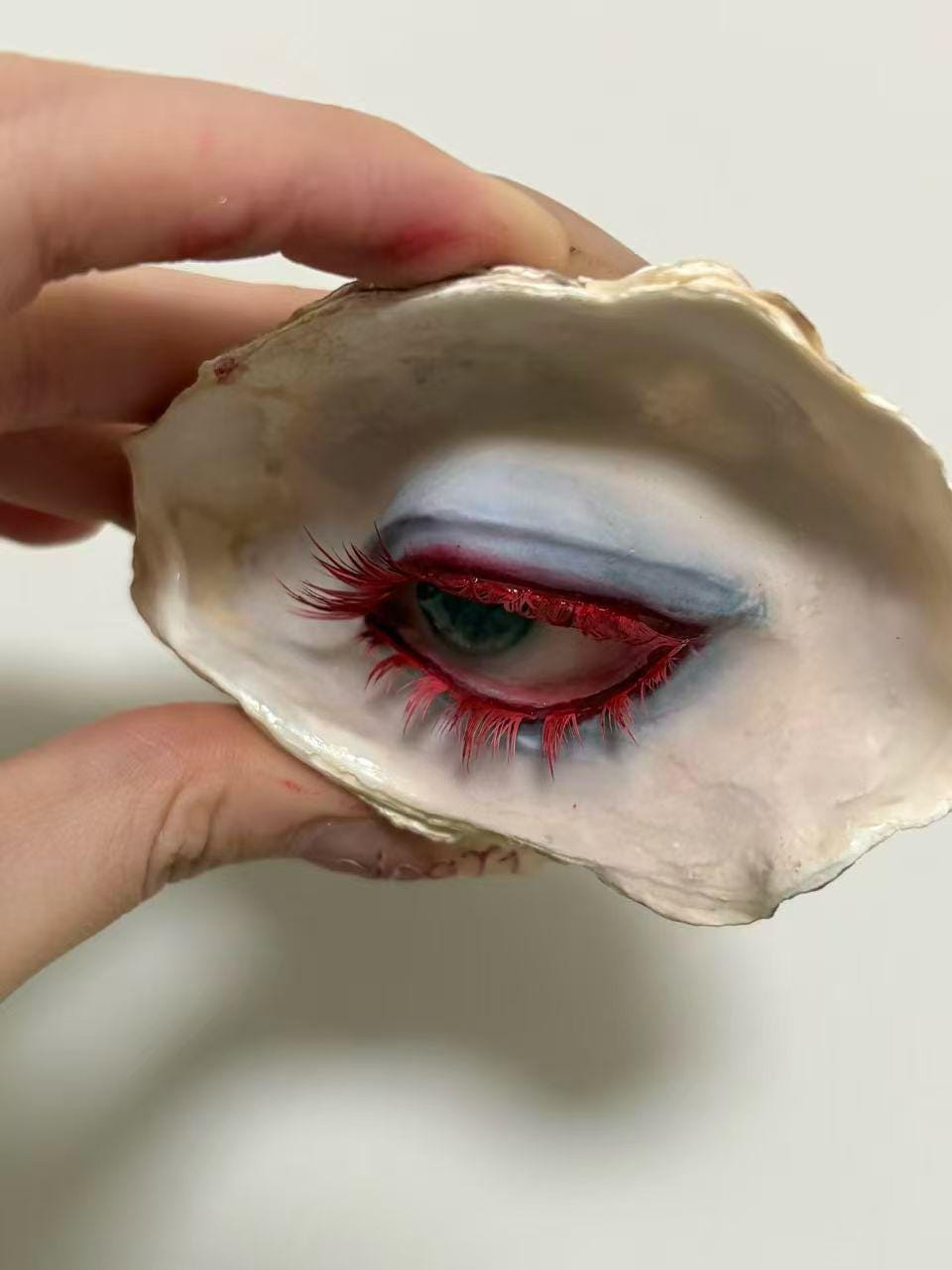 Red-Lash Oyster Eye held in a hand, showing red lashes and cool-toned smoky makeup.