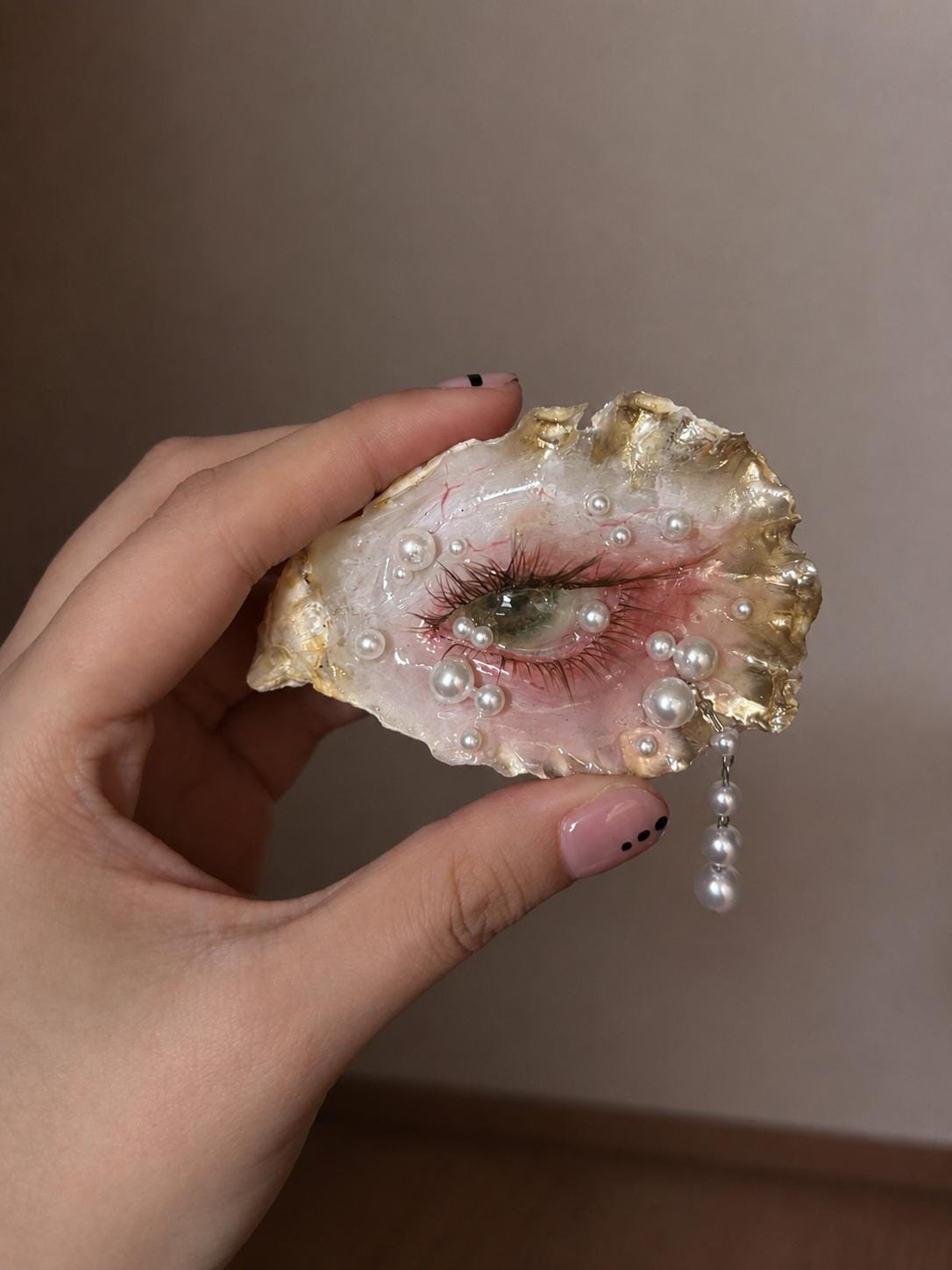 Close-up of Gilded Oyster Eye held in a hand, showing the green iris and gold-toned shell edge.