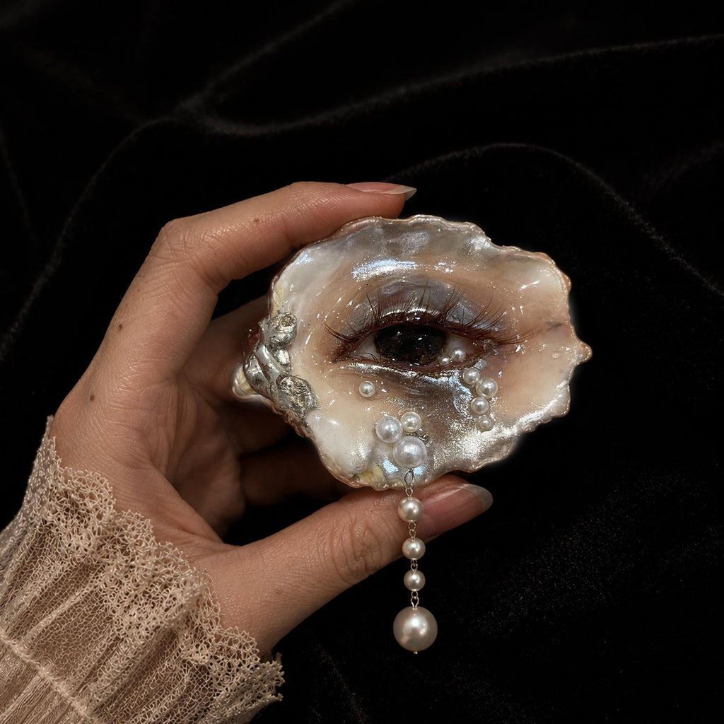 Brown Smoky Oyster Eye brooch held in a hand to show its scale and dangling drop.
