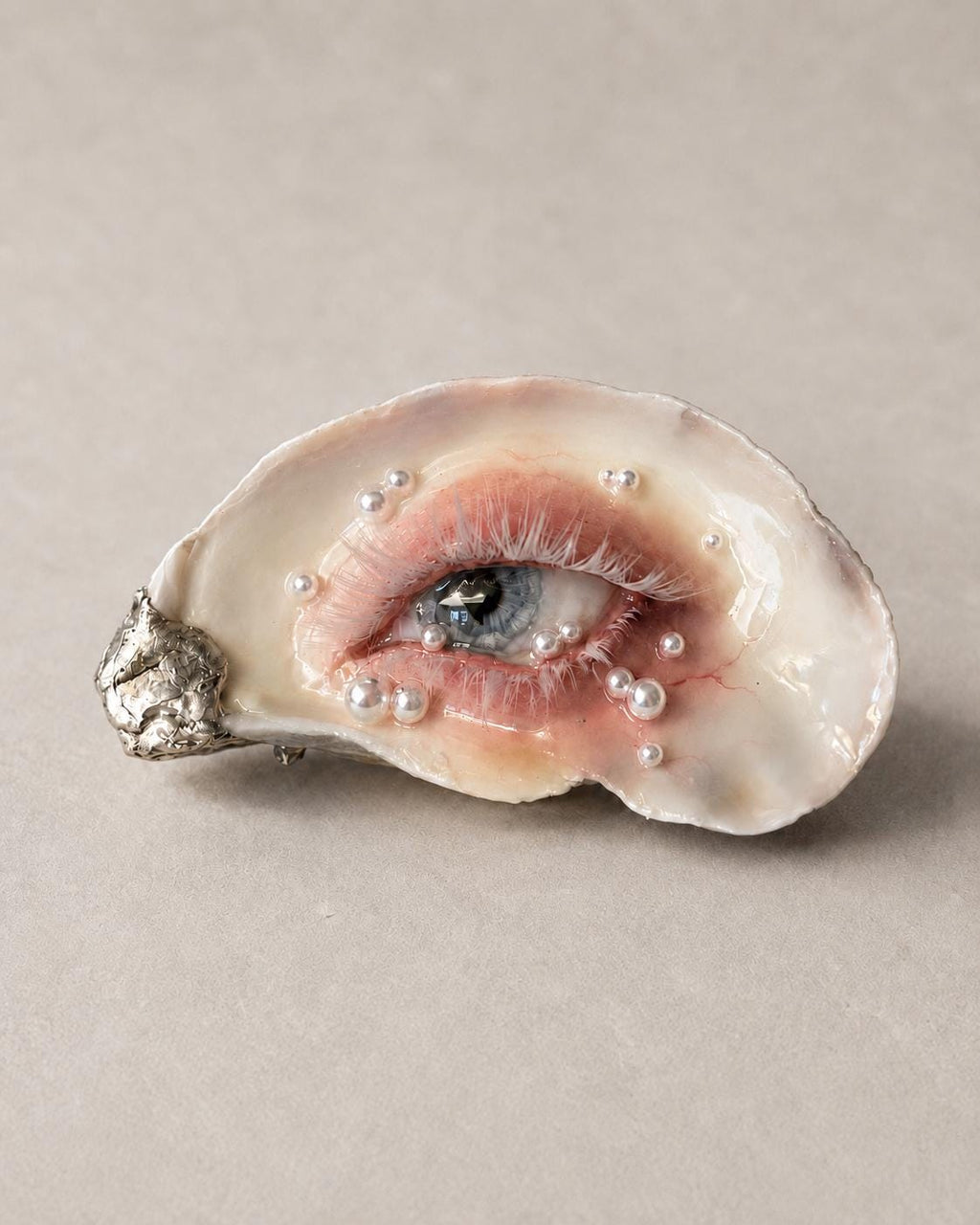 Blue-eye oyster-shell artwork resting on a pale surface, showing the iris and fine lashes.
