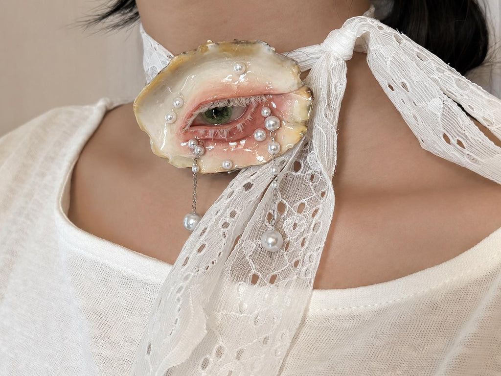 Close-up of Green-and-Gold Oyster Eye worn on white lace ribbon.