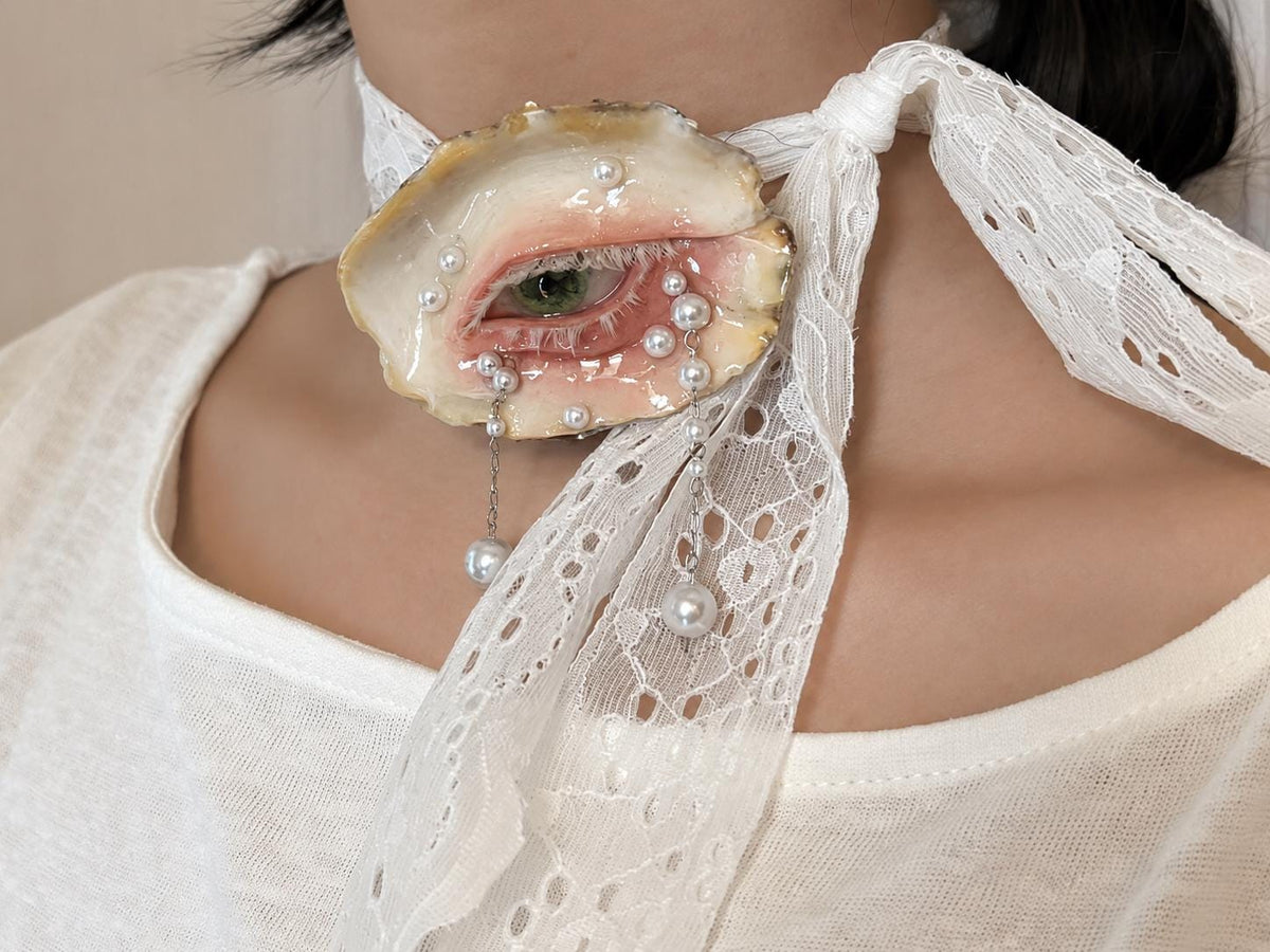 Close-up of Green-and-Gold Oyster Eye worn on white lace ribbon.