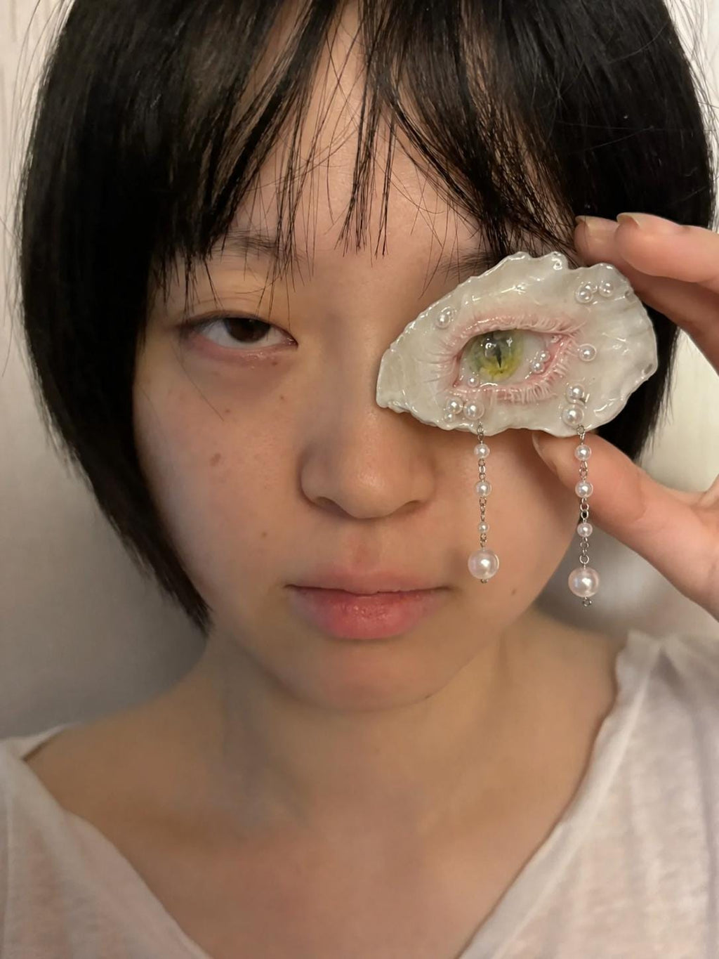 Cat-Eye Green Pupil shell-eye piece held beside a model's face above a white shirt.