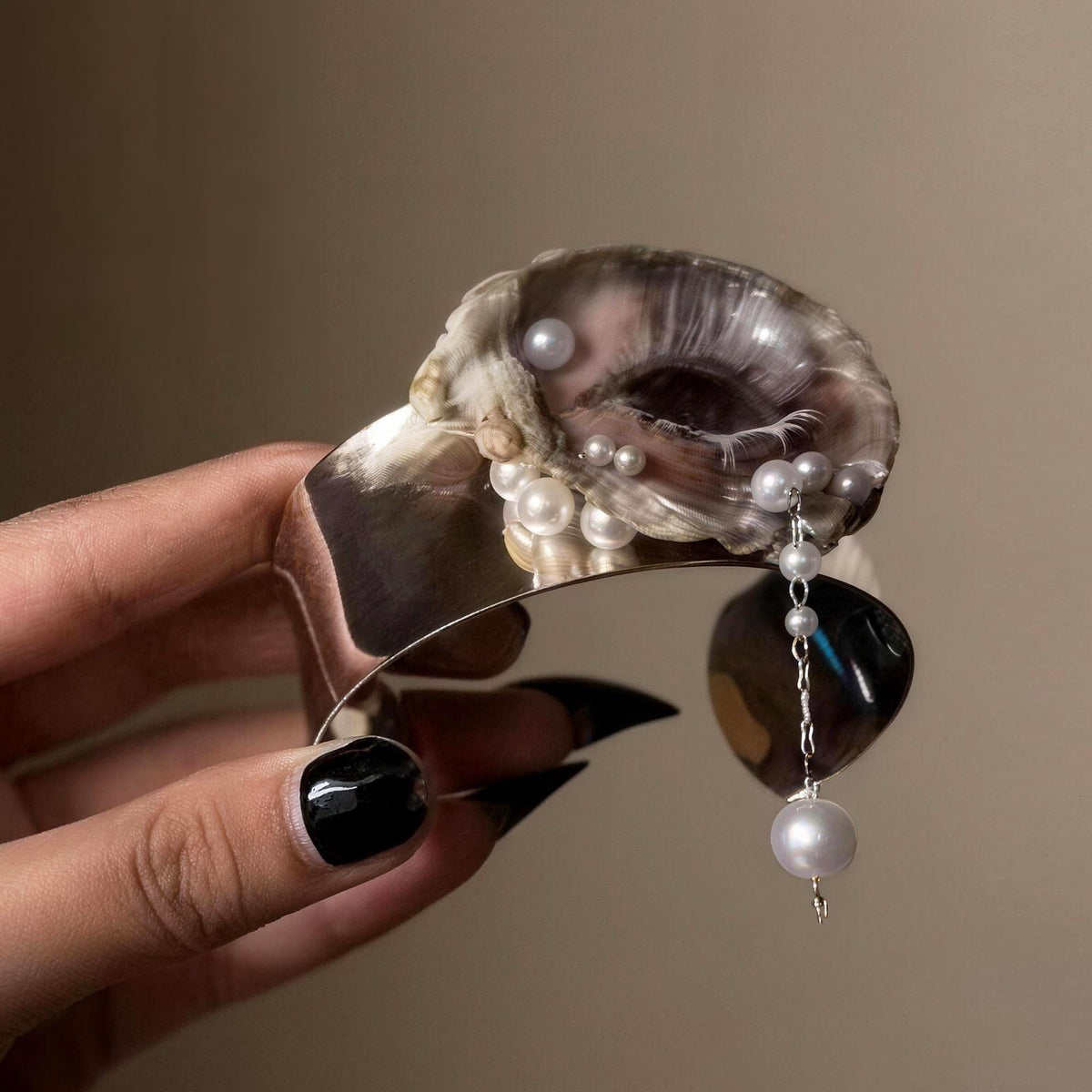 Gilded Oyster Eye Cuff Bracelet held to show the open metal band and shell-eye centerpiece.