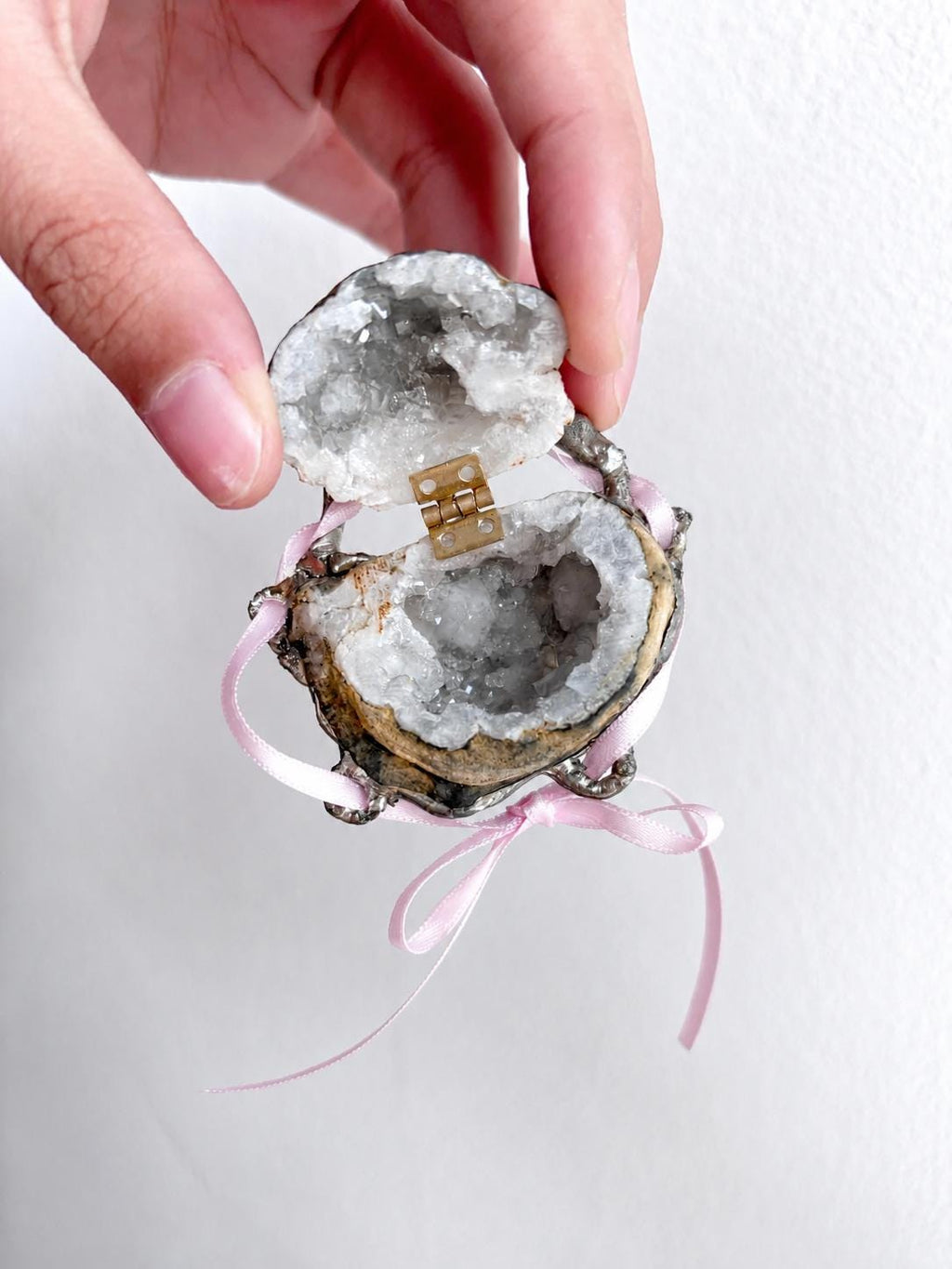 Open Geode Shell Trinket Box with grey crystal texture and pink ribbon, held against a light wall.