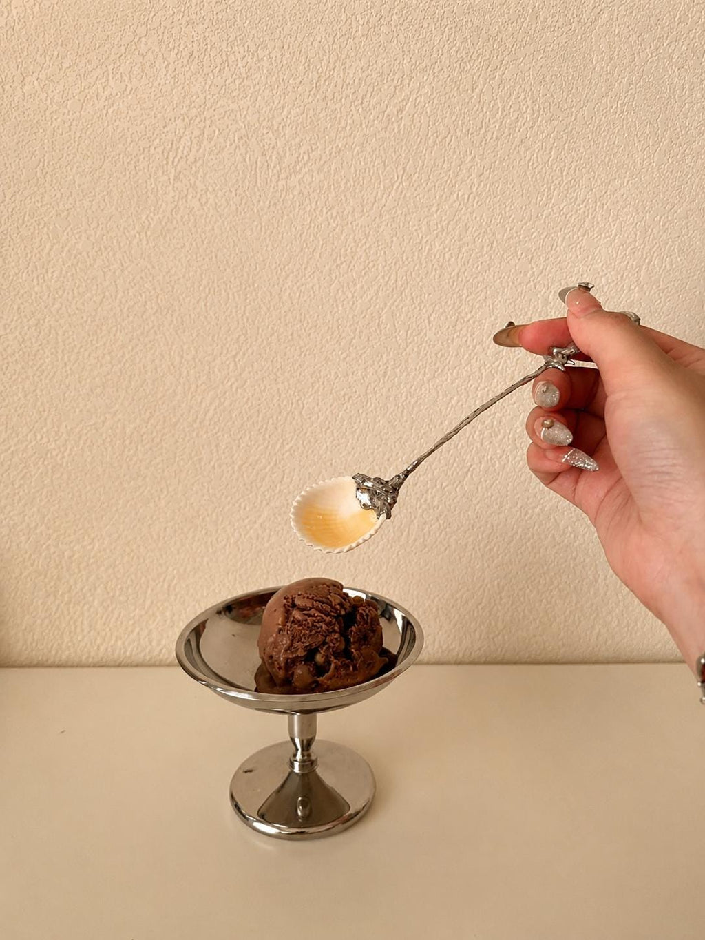 Decorative shell spoon shown above a small plated cake in a styling scene.