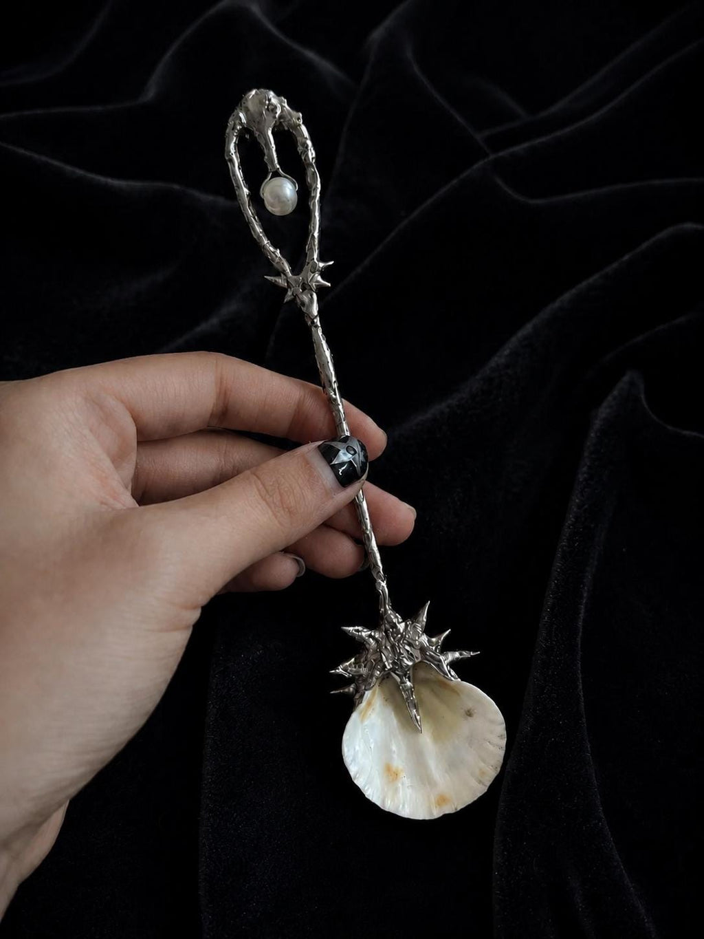 Decorative shell spoon with an openwork loop handle and pale shell bowl, held against black fabric.