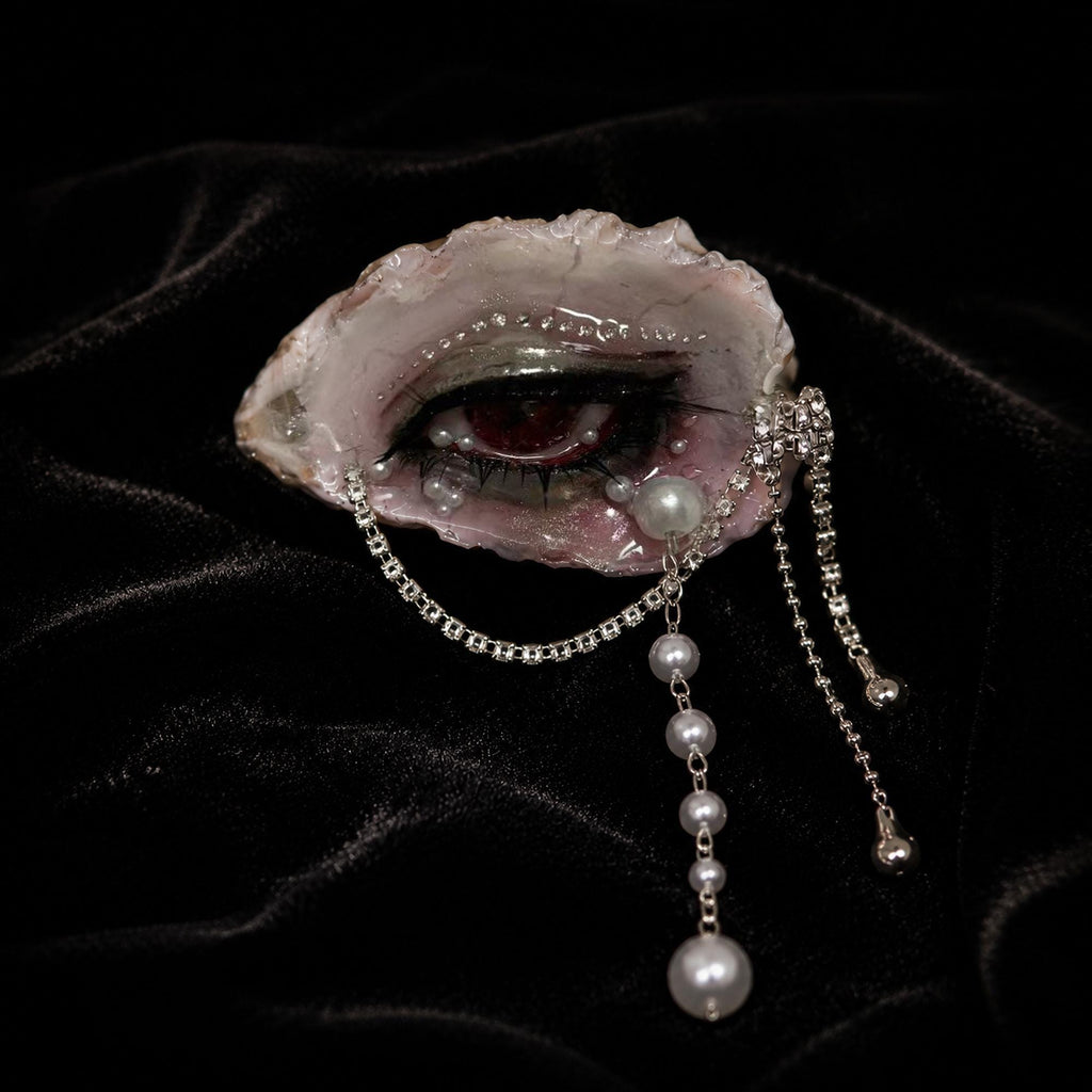 Lilith Veil oyster eye on black velvet showing red pupil, faux pearls, and silver chains