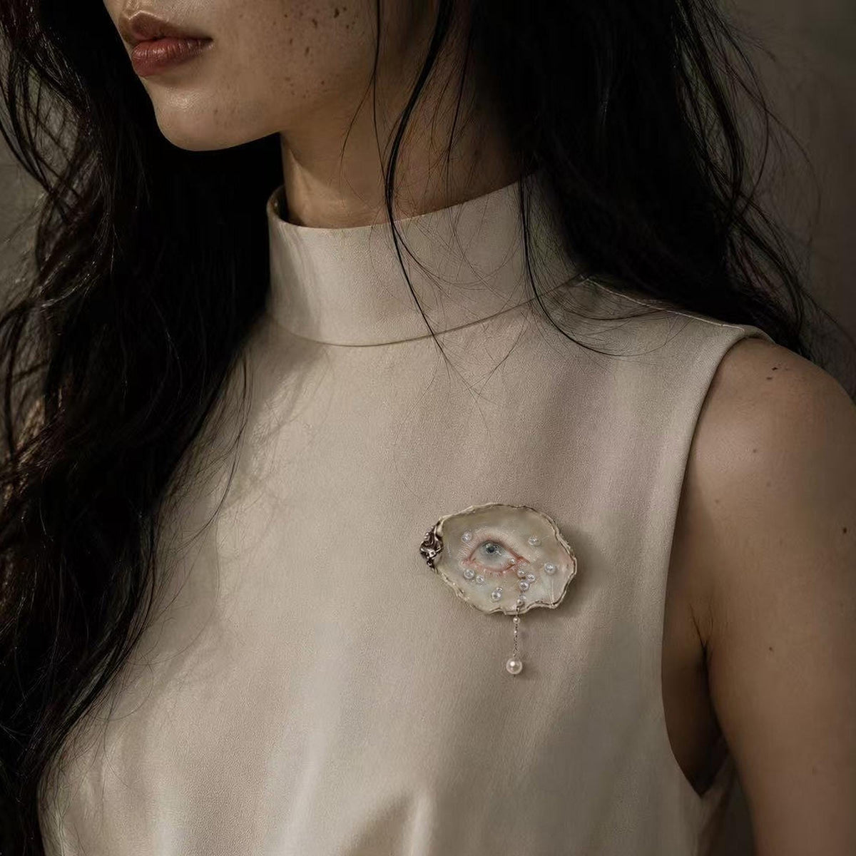 Nyra Unimpressed Gaze shell-eye brooch worn on a sleeveless cream top.