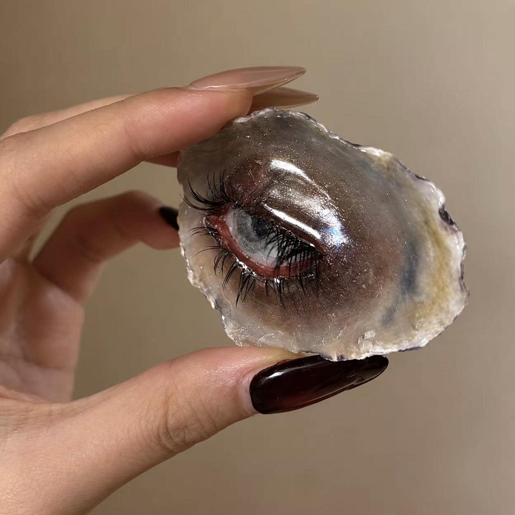 Angled hand-held view of Lilith Grey Temptation showing the sculpted eyelid and shell depth.