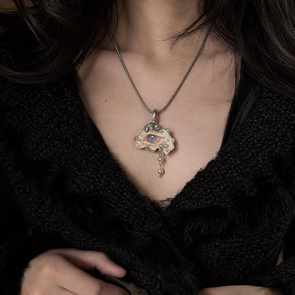 Nyra shell-eye necklace worn on a fine metal chain over a black lace top.