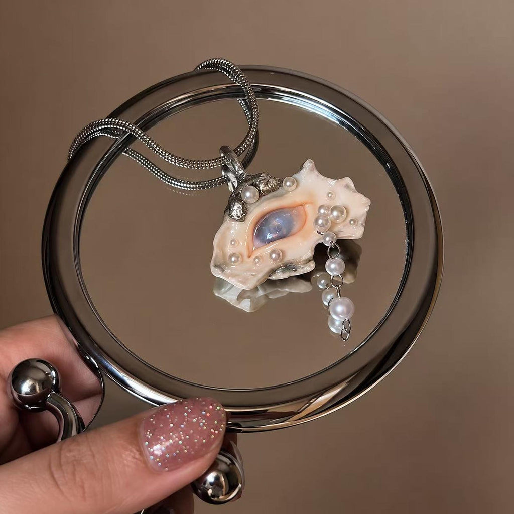 Nyra shell-eye necklace held beside a round metal display ring.