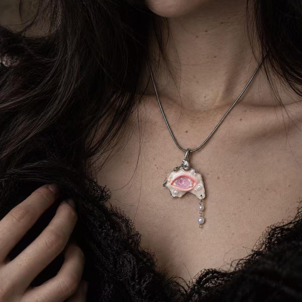 Pink-eyed Nyra shell pendant with a hanging bead drop worn on a metal chain.