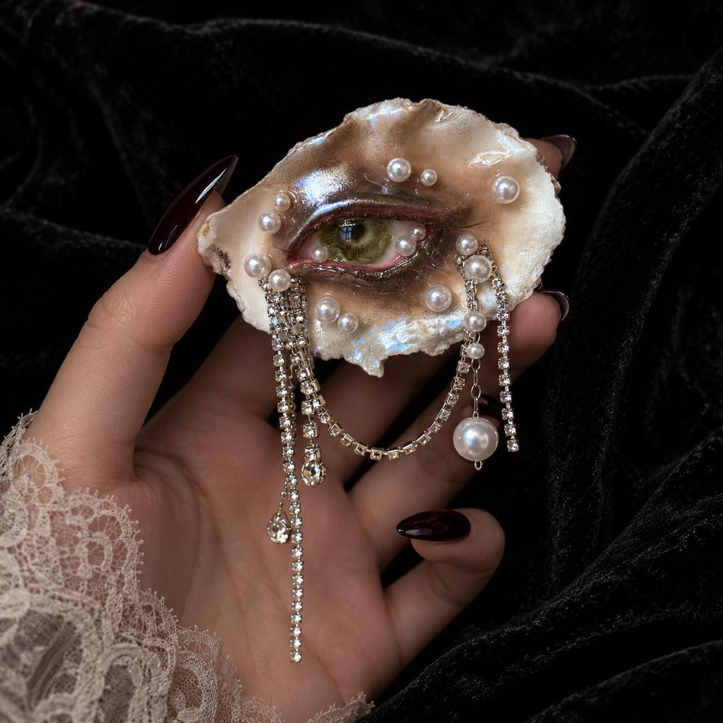 Lilith Veil Emerald Siren oyster eye with a green iris and draped bead chains, held in a hand.