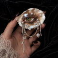 Lilith Veil Emerald Siren oyster eye with a green iris and draped bead chains, held in a hand.